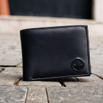 **

A close-up shot of a well-worn Stone Island wallet, showcasing its premium leather texture and meticulous stitching. Focus on the iconic Stone Island patch, subtly placed. The wallet is slightly open, revealing a few essential cards and a small amount of cash. The background is a blurred, urban setting, suggesting a stylish, on-the-go lifestyle. The overall feel is understated cool and high quality.

**