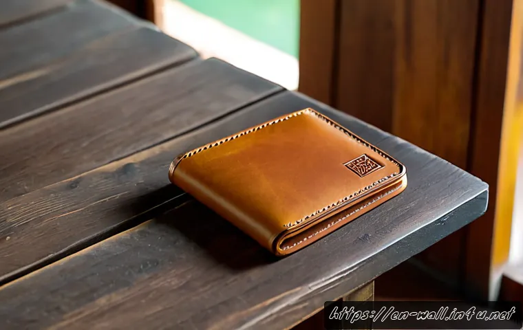 발리 가죽 지갑의 내구성과 스타일 - Photorealistic close-up of a handcrafted tan leather bifold wallet resting on a weathered teak table...